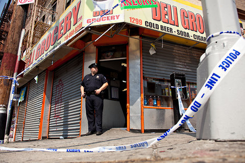 An officer standing outside the deli in the Bronx where a worker was fatally shot by the police. Photo by Uli Seit for The New York Times